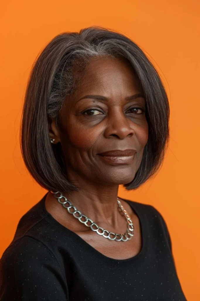 Senior Black woman sporting a chic blunt shoulder cut with gray hair, an elegant medium length hairstyle for women over 60, set against an orange background.