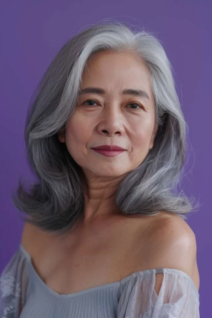 Elderly woman with a long bob and side bangs, a stylish medium length hairstyle for women over 60, against a violet backdrop.