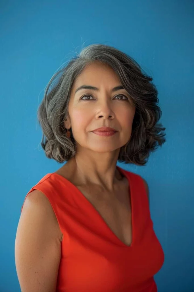 Senior woman in red dress with a medium choppy bob hairstyle, perfect for women over 60 looking for a fresh, medium-length style, against a blue background.