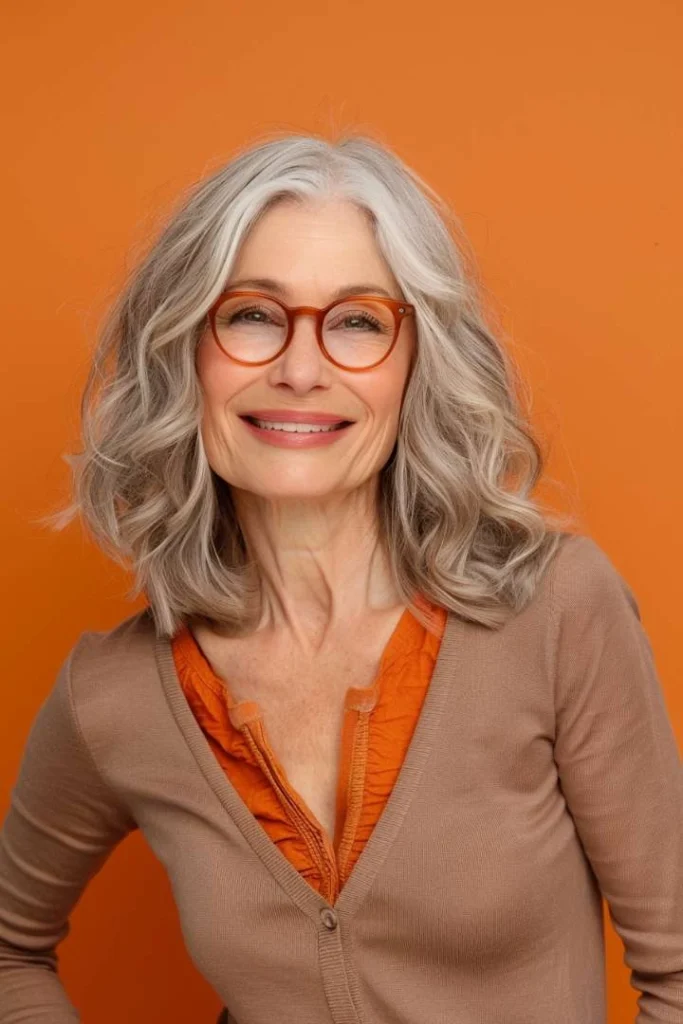 Mature woman with voluminous layered hair, a vibrant medium length hairstyle for women over 60, smiling in an orange setting.